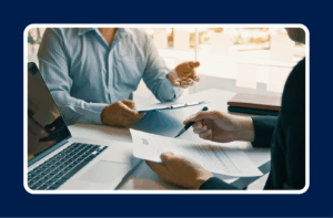Two people sitting together at an office table with papers in hand.