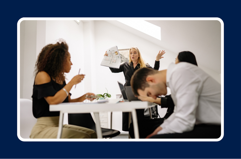 A tense office meeting showing visible conflict: a frustrated woman standing and gesturing with building plans in hand, while a man at the table rests his head in stress and others look disengaged. Illustrates a workplace disagreement and the need for strategies on how to handle conflict at work.
