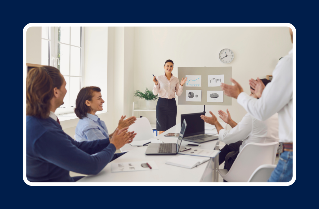 A first-time manager giving a presentation to colleagues in a meeting room, with charts and graphs displayed on a board and team members clapping.