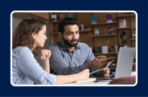 Two professionals in a discussion reviewing documents and a laptop screen, illustrating a collaborative approach to skills-first hiring in the workplace.