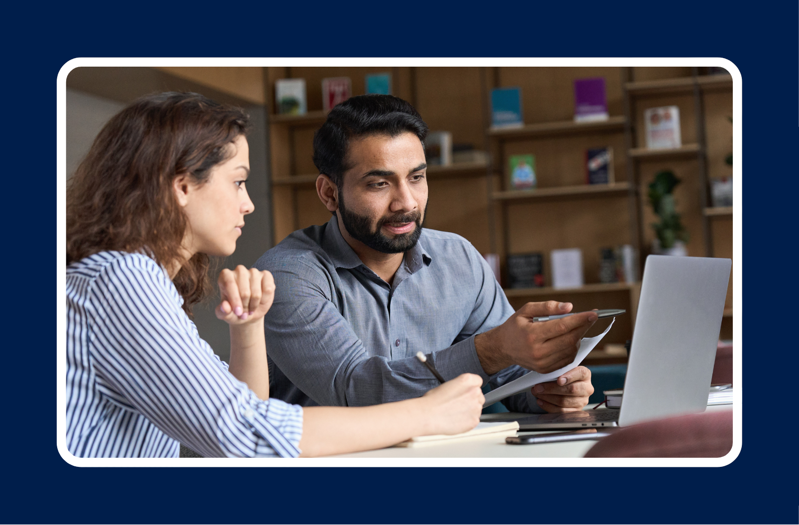 Two professionals in a discussion reviewing documents and a laptop screen, illustrating a collaborative approach to skills-first hiring in the workplace.