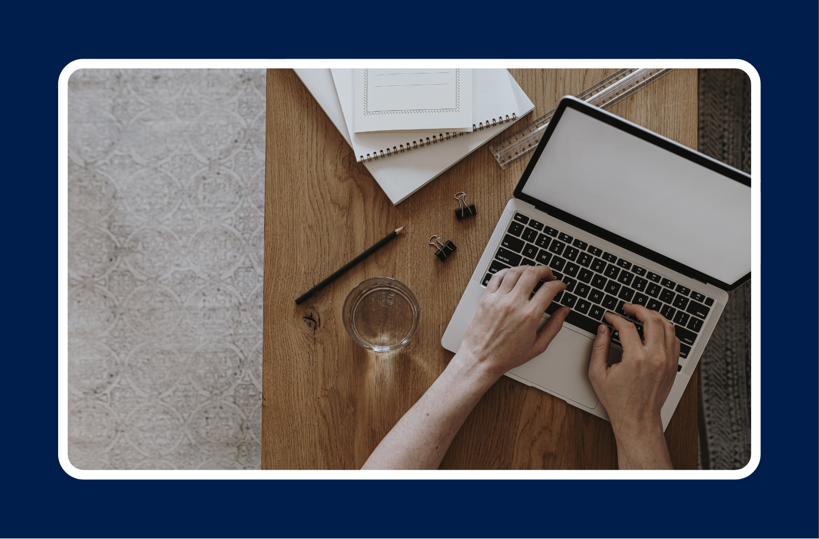 Person working on a laptop at a wooden desk with notebooks, pencil, and glass of water, representing remote work in full-time vs contract IT employment.