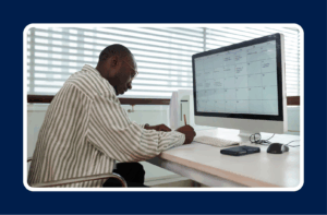 An executive planning the best work schedule for your team, reviewing a digital calendar on a computer while taking notes at a desk.
