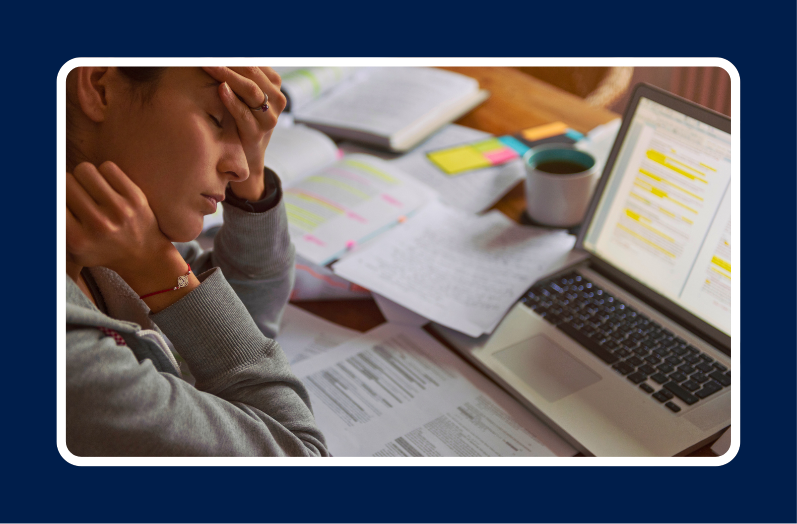 A stressed employee sitting at a desk with a laptop, notes, and coffee, holding their head in frustration, illustrating the importance of learning how to prevent burnout at work.