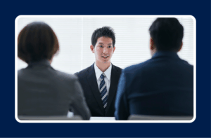 A professional man in a business suit speaks confidently during an interview with two hiring managers, representing the application of mid-career transition tips for job seekers.