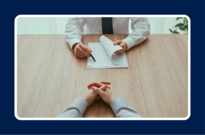 A hiring manager reviews a candidate’s resume during an interview, holding a pen and papers across a wooden table — representing the process of identifying IT candidate red flags in technical hiring.
