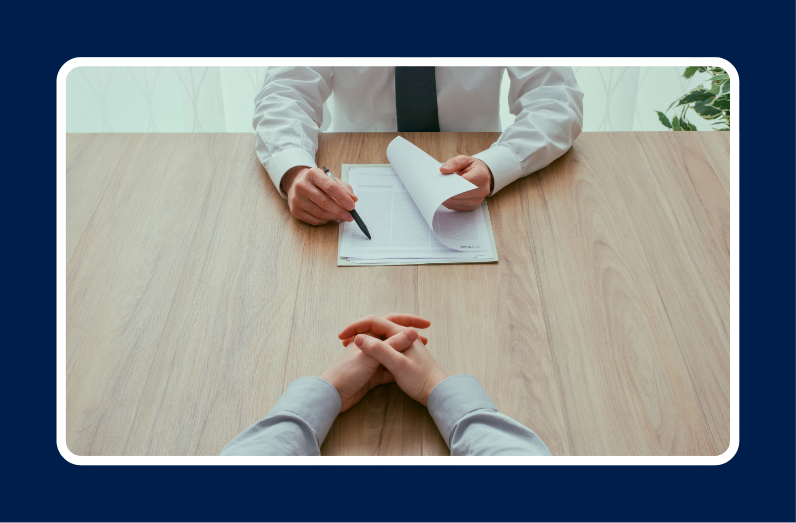 A hiring manager reviews a candidate’s resume during an interview, holding a pen and papers across a wooden table — representing the process of identifying IT candidate red flags in technical hiring.