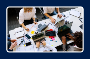 tech team collaborating around a table with laptops, representing imposter syndrome in tech teams and the importance of psychological safety