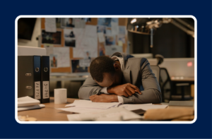Exhausted office employee asleep at a cluttered desk late at night, illustrating common employee burnout warning signs such as fatigue, stress, and overwork in the workplace.
