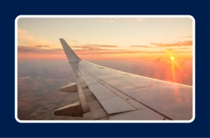 Airplane wing viewed from a passenger window during a summer sunset, with warm golden light illuminating the sky above the landscape below. This travel-themed image represents taking time away from work and offers a visual for discussions on how to prepare for PTO, vacation planning, and ensuring a smooth transition before taking leave.