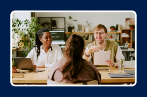 Hiring leaders discussing internal mobility vs. external hiring during a candidate interview at a wooden conference table, with a laptop and resume in view.