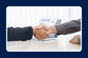 Two business professionals shaking hands across a desk, representing a hiring decision and the importance of understanding the cost of a misaligned hire.